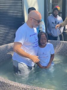 A person being baptized in a water tank with another individual assisting.