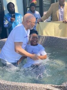 A person being baptized in a font by another individual while witnesses observe.