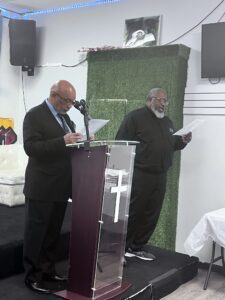 Two men reading from papers at a lectern in a room with christian religious symbols.