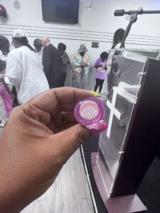A person holding a pink personal handheld fan at a gathering where several people are standing and conversing in the background.
